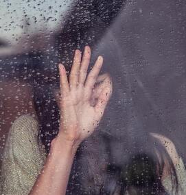 Woman with palm against rainy window